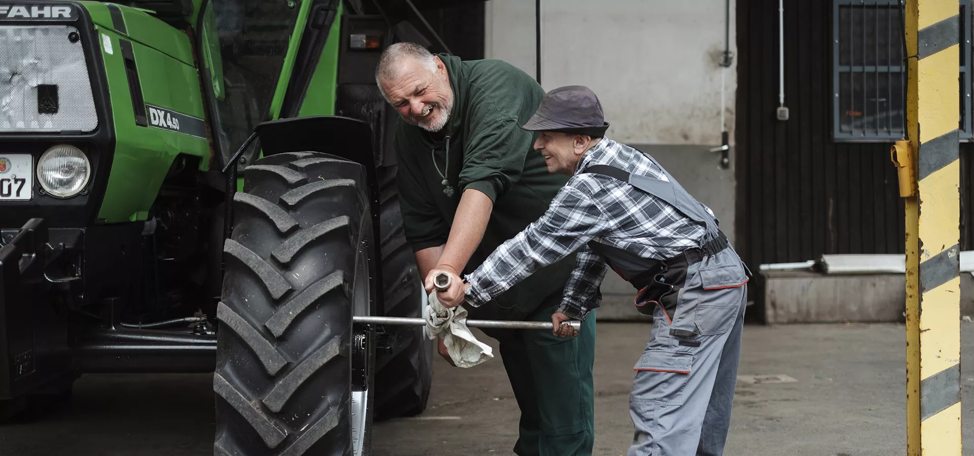 Ein sehr großer und ein sehr kleiner Mitarbeiter ziehen die Schrauben an dem Reifen eines Treckers fest.